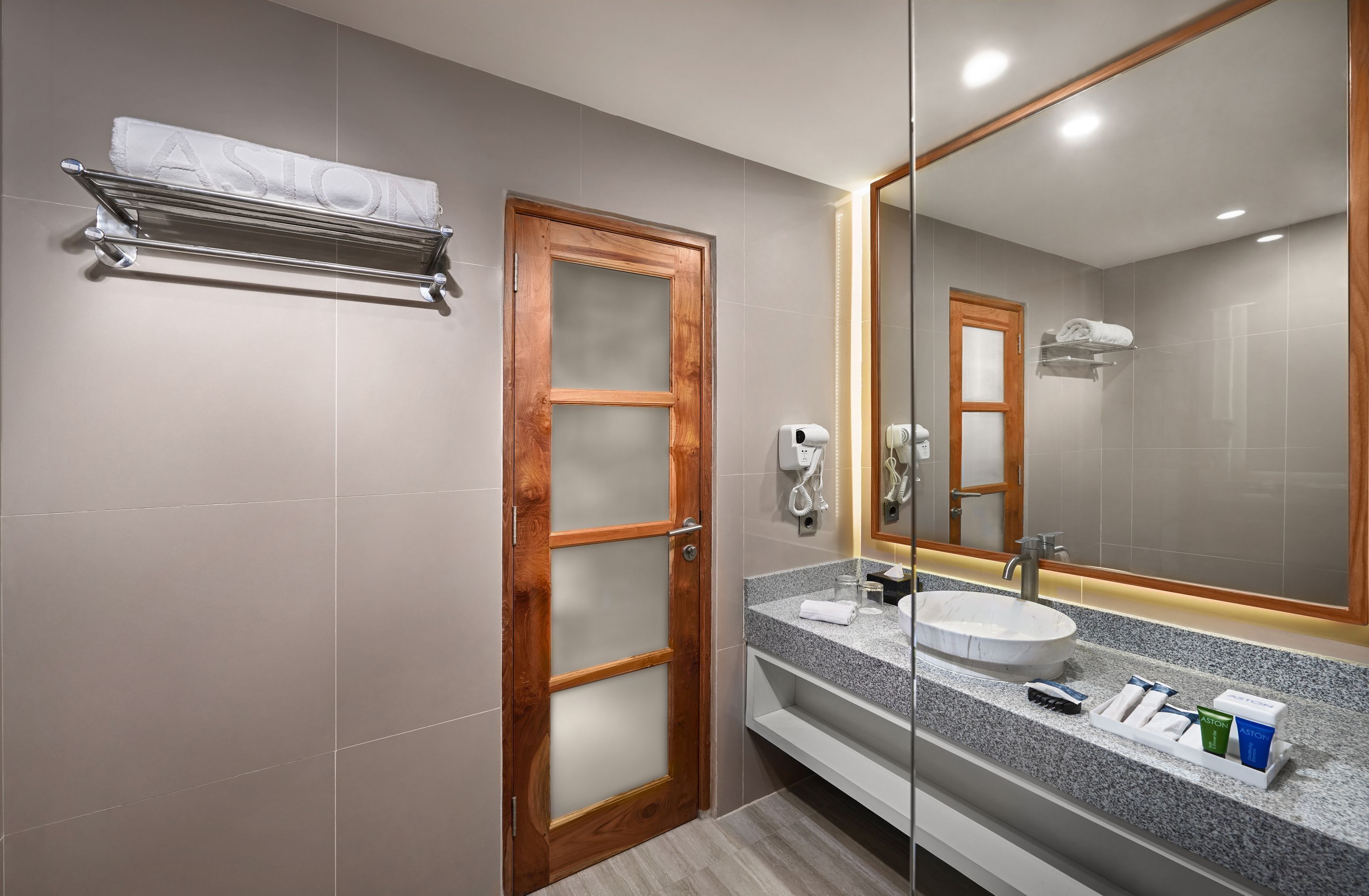 A modern bathroom with a wooden door, a large mirror, a sink, and a towel rack.
