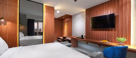 Une chambre d’hôtel moderne dotée d’un grand lit, d’un bureau avec un téléviseur à écran plat et d’un coin salon avec un fauteuil bleu.