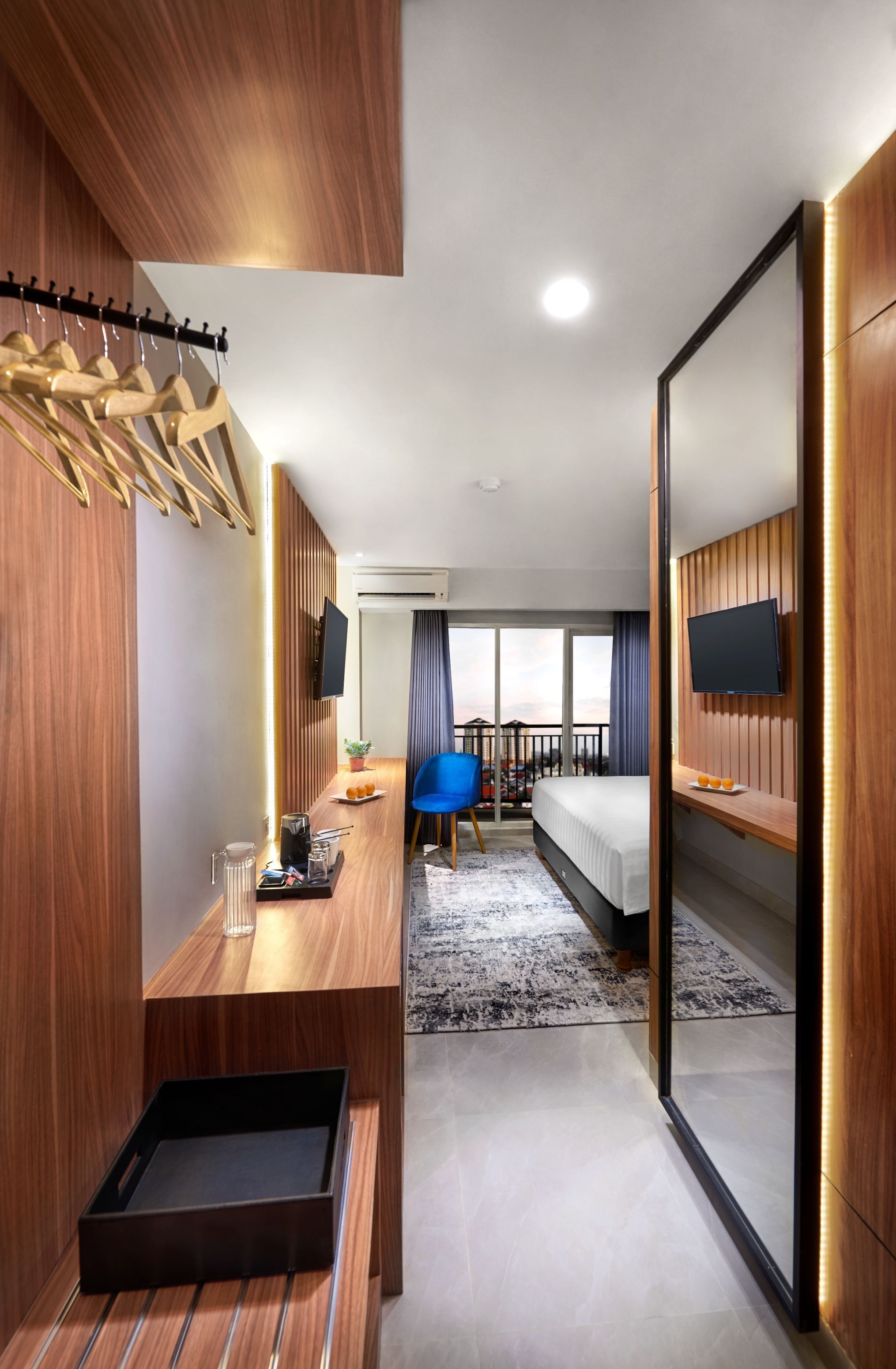 A modern hotel room with a wooden accent wall, a large bed, a desk with a chair, a TV, and a balcony with a view.