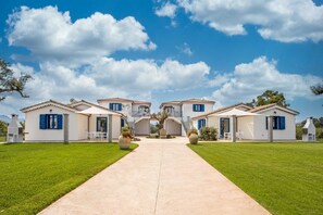 A villa with a central archway, multiple rooms with blue shutters, and a well-maintained lawn.