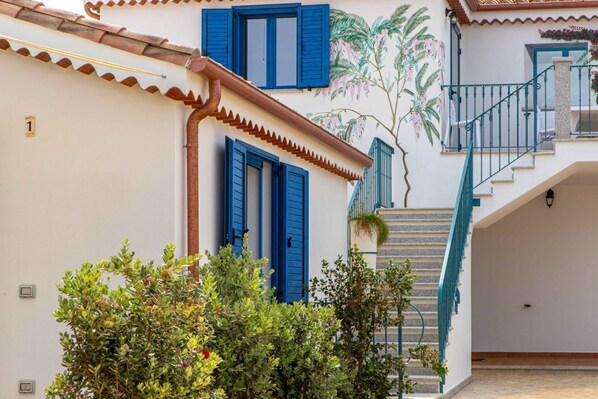 A building with blue shutters, a staircase, and a mural of a palm tree.