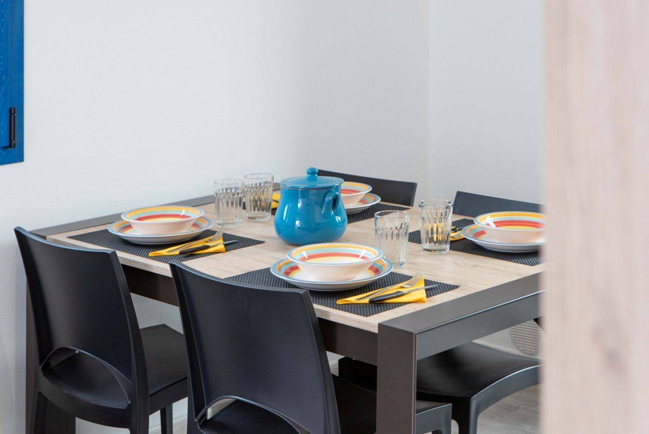 Una mesa de comedor dispuesta con platos, vasos y una tetera azul.