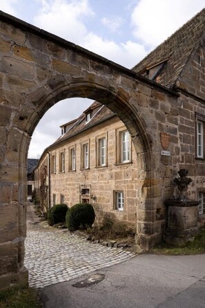 A stone archway leading to a building with multiple windows and a cobblestone path. - Gutsverwaltung Schloss Eyrichshof (Ebern)
