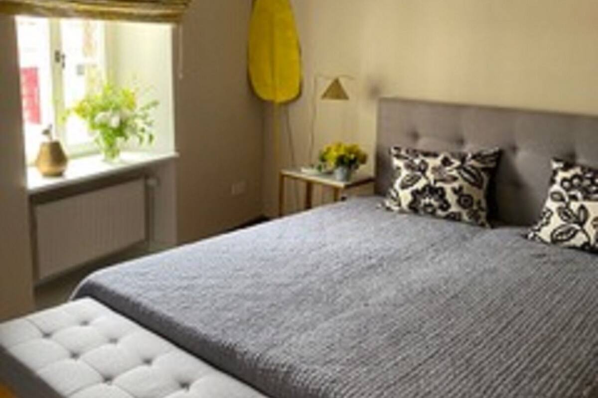 Un dormitorio con una cama grande, una ventana con persiana amarilla y una mesita de noche con lámpara.