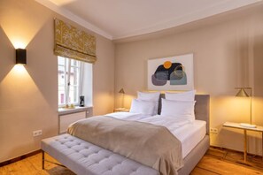Une chambre à coucher avec un lit, des tables de chevet, une fenêtre avec des rideaux, un radiateur et un tableau accroché au mur.