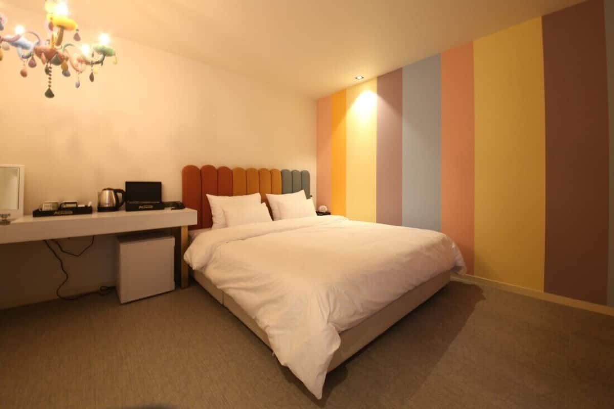 Una habitación de hotel con una cama, un escritorio con un ordenador, un refrigerador pequeño y una pared colorida.