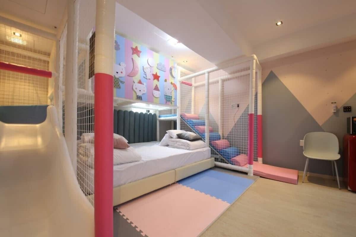 Zona de juegos infantiles con tobogán, colchonetas blandas y una cama con almohadas.