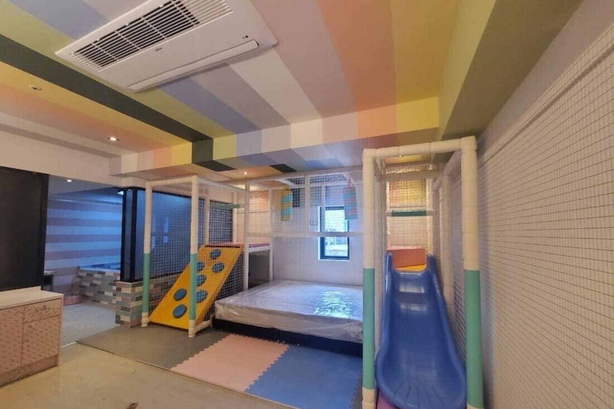 Zona de juegos infantiles con tobogán, red de escalada y suelo acolchado.
