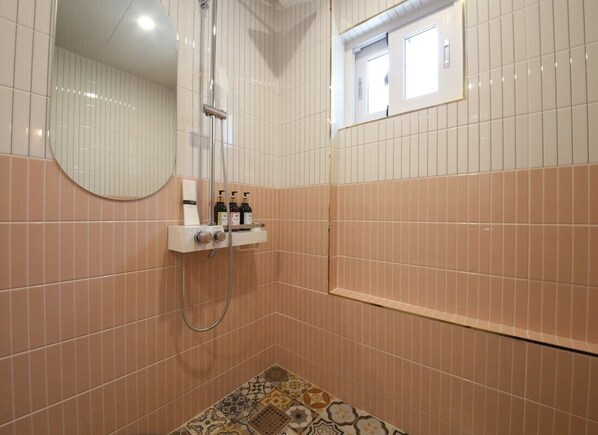Un baño con ducha, espejo y estante con artículos de aseo.