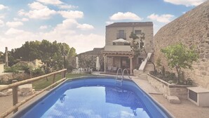 Una piscina con plataforma de madera y pared de piedra.