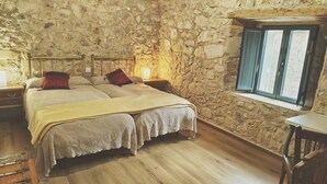 Un dormitorio con pared de piedra, una cama de madera, una mesita de noche y una ventana con persianas.