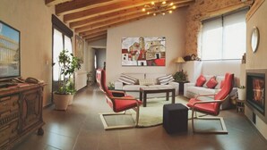 Un salón amplio con chimenea, un sofá, una mesa de centro y sillas rojas. Hay un cuadro en la pared y un techo de madera.