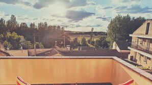 Una terraza en la azotea con dos sillones rojos acolchados, una mesita con una botella y una copa de vino, y vistas a una zona residencial con árboles y edificios.