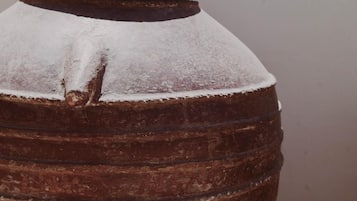 Un grand pot en terre cuite, de style rustique, avec une base large et un sommet étroit, posé sur une surface plane, adossé à un mur uni.