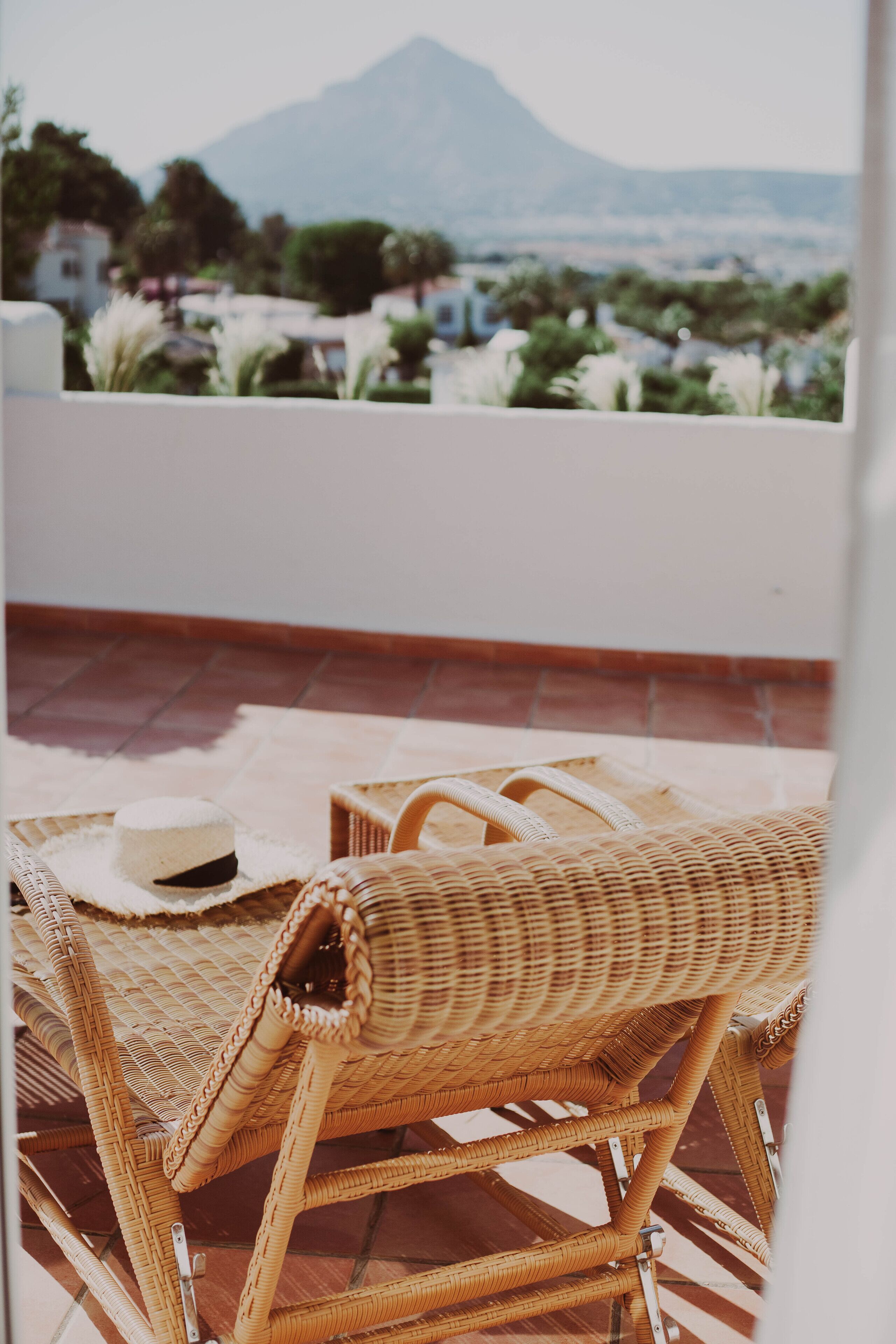 A wicker chair and table on a terrace with a mountain view.