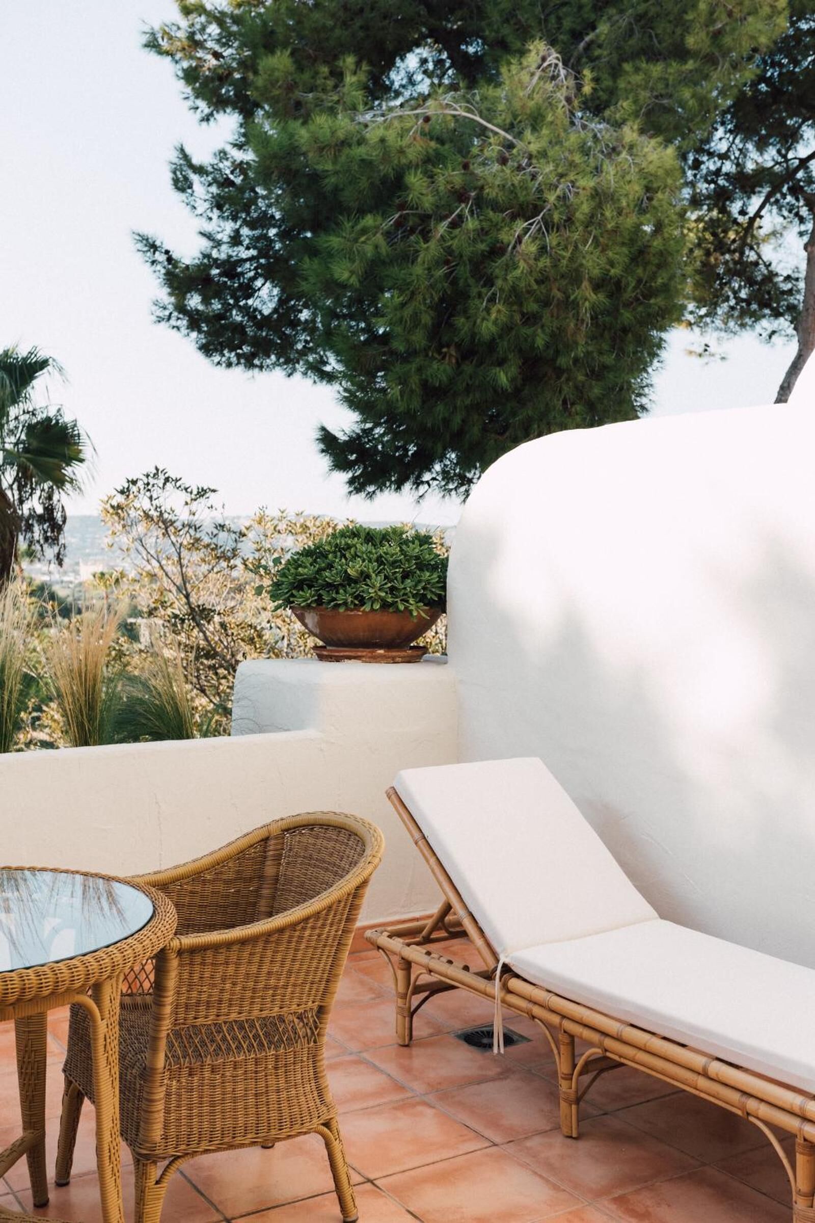 A patio with wicker furniture, a white cushioned lounge chair, and a glass table.