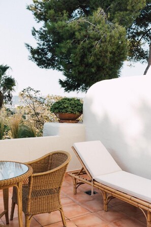 A patio with wicker furniture, a white cushioned lounge chair, and a glass table.