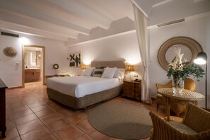 A bedroom with a large bed, bedside tables, a round wicker table, and a mirror.
