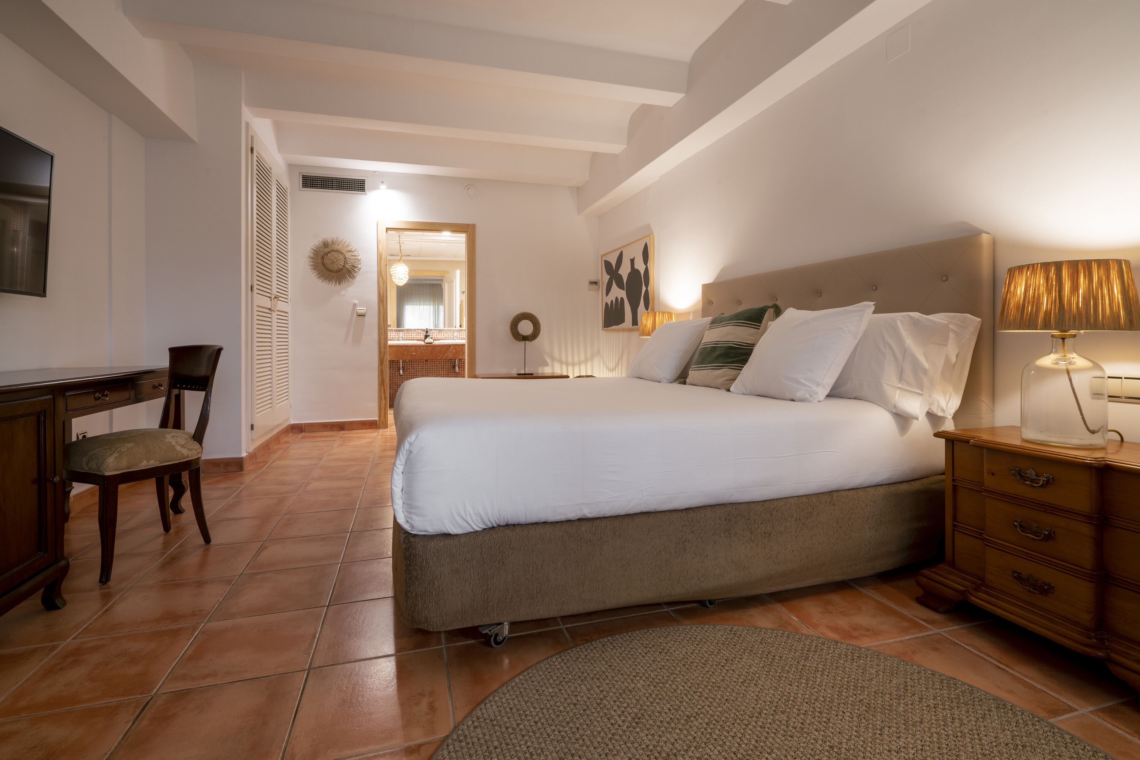 Un dormitorio con cama, escritorio, silla, mesita de noche y lámpara.