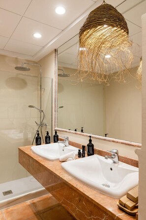 A modern bathroom with two sinks, a large mirror, and a unique woven light fixture.