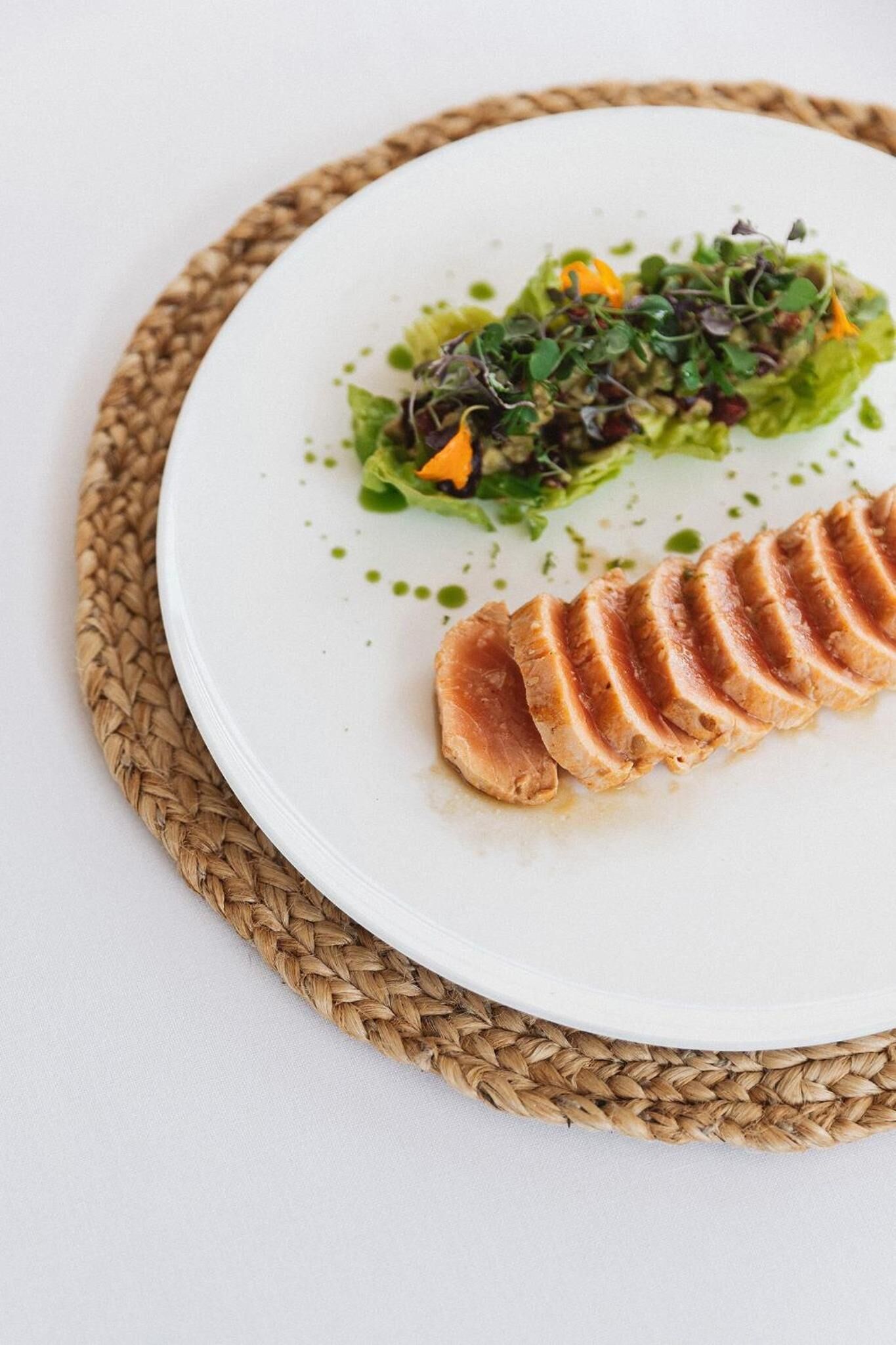 A white plate with sliced meat and a green salad on a woven placemat.