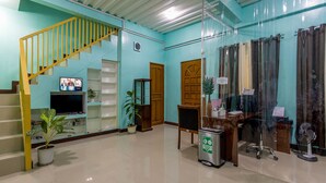 A spacious room with a staircase, a television, a desk with a computer, a fan, and a trash bin. - OYO 805 La Belladoza (Parañaque)