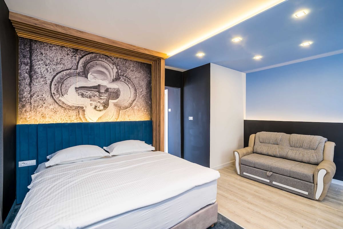Une chambre à coucher comprenant un lit, un canapé, une œuvre d’art accrochée au mur et un éclairage encastré au plafond.