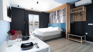 A modern hotel room with a bed, a dining table with cutlery, a wine glass, and a view of the city. - Apartments Tayra (Dubrovnik)