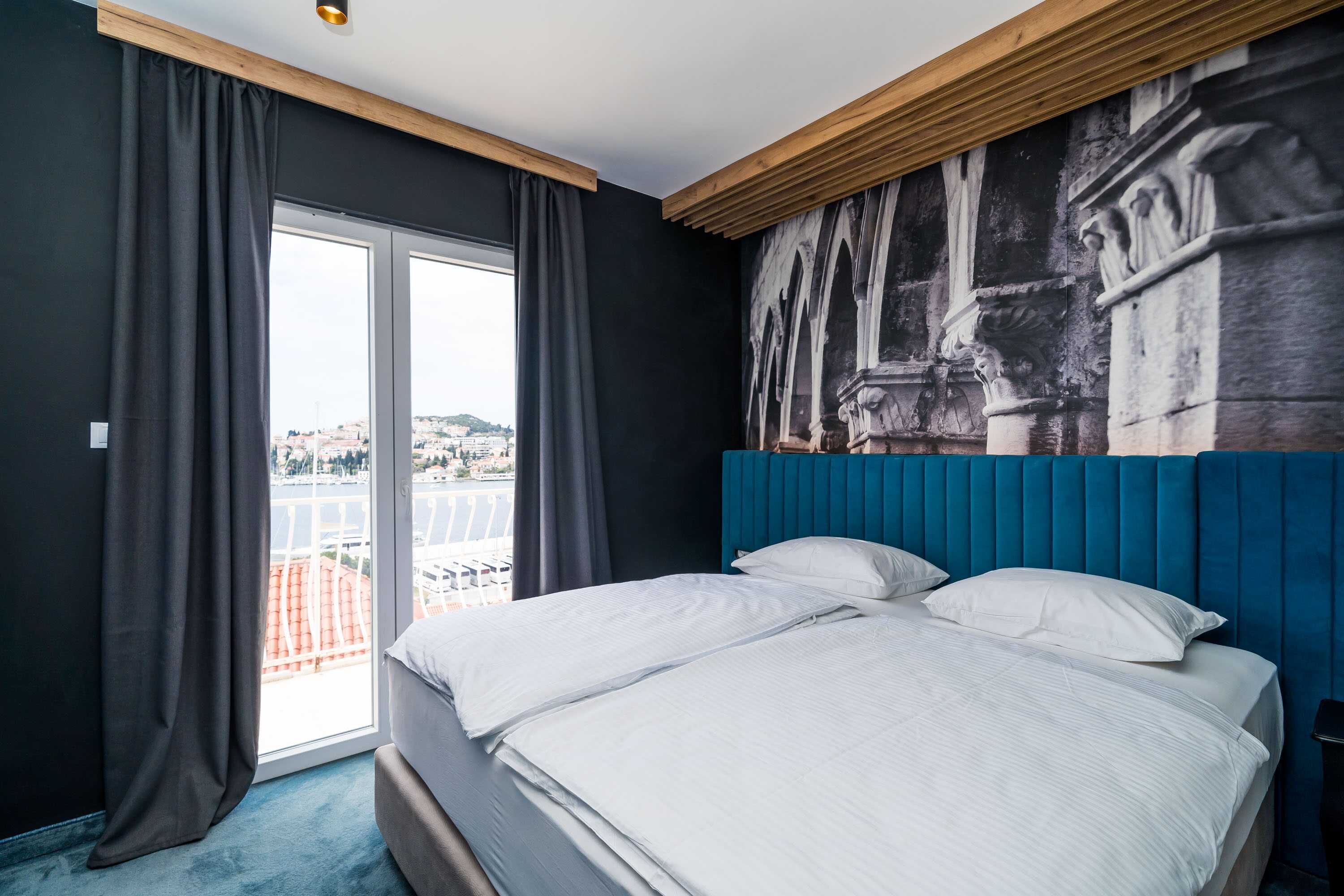 Habitación de hotel con una cama grande, vista a la ciudad por una ventana y un mural en la pared.