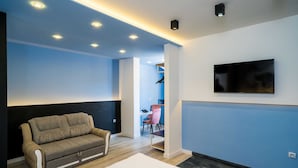 A modern living room with a sofa, a flat-screen TV mounted on the wall, and recessed ceiling lighting. - Apartments Tayra (Dubrovnik)