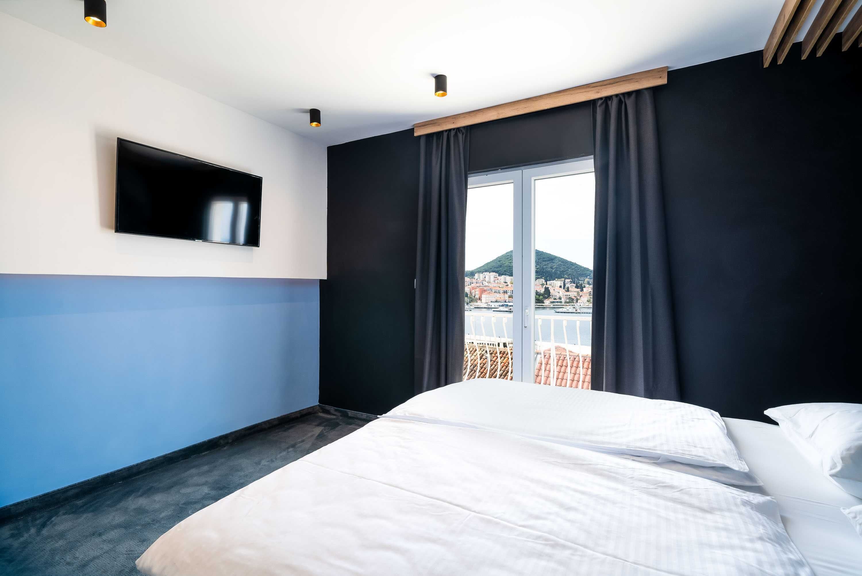 A hotel room with a bed, a TV mounted on the wall, and a view of a cityscape through the window.