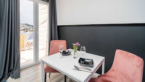 A dining table with two chairs, a vase with flowers, and a city view through a glass door. - Apartments Tayra (Dubrovnik)