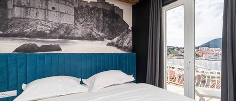 A hotel room with a bed, a view of a historic stone wall, and a balcony with a railing.