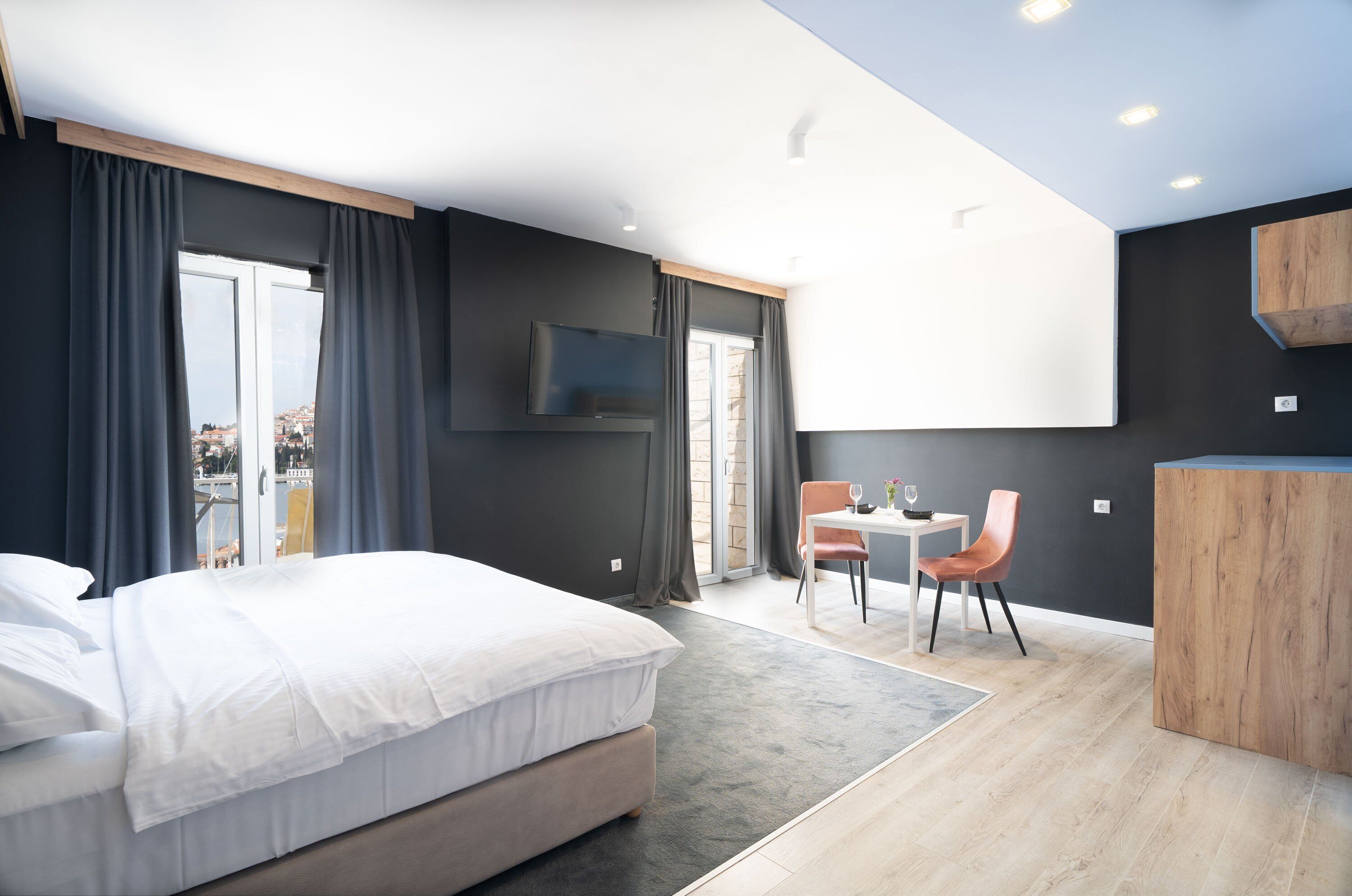 Una habitación de hotel moderna con una cama grande, una zona de comedor con mesa y sillas, y un televisor fijado en la pared.