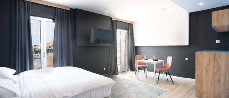 Una habitación de hotel moderna con una cama grande, una zona de comedor con mesa y sillas, y un televisor fijado en la pared.