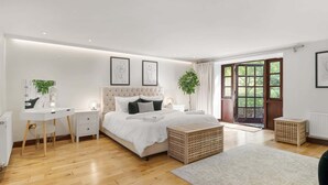 A modern bedroom with a large bed, bedside tables, a vanity with lights, a large window with a view, and a door leading to an outdoor area.