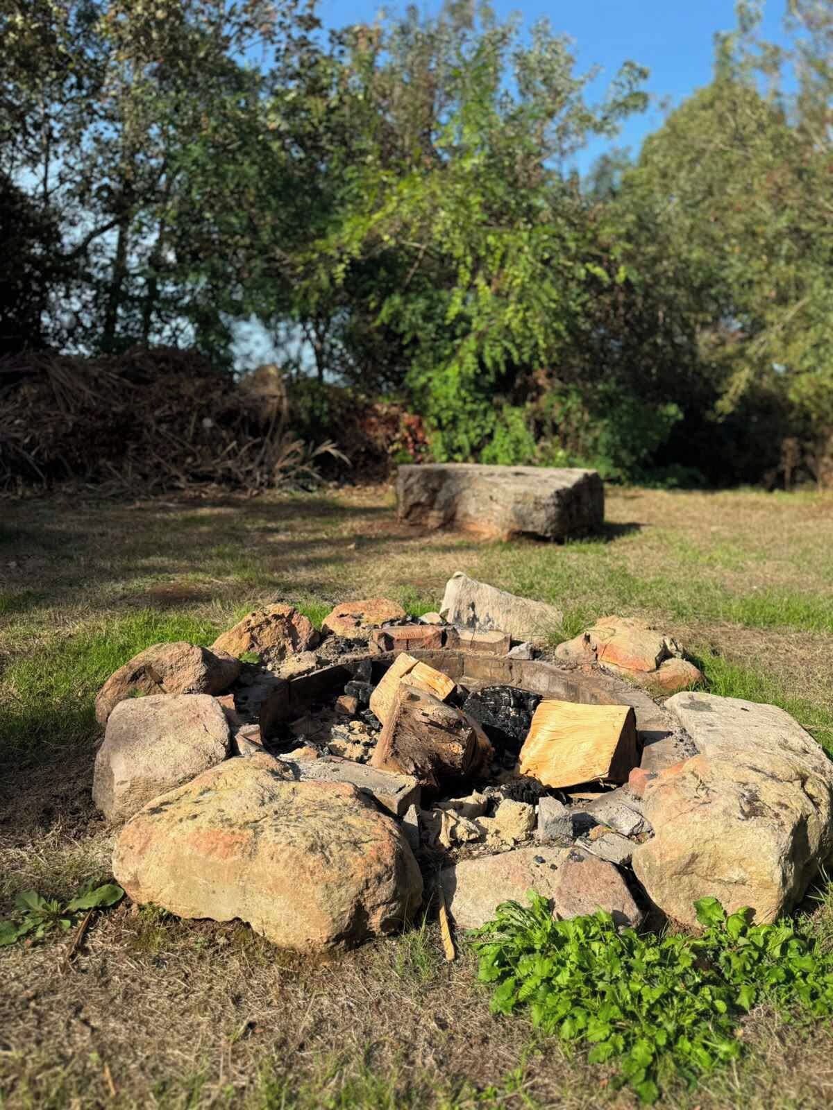 A campfire surrounded by rocks in a grassy area with trees in the background.