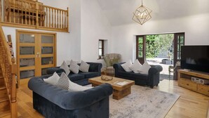A spacious living room with a staircase, a large wooden cabinet, two sofas with patterned cushions, a coffee table, and a television.