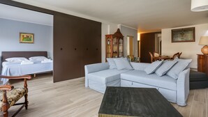 A modern hotel room with a light blue sofa, a wooden chair, a dark coffee table, a bed with white linens, and a wooden cabinet with glass doors. - Stunning view over Ponte Vecchio (Firenze)