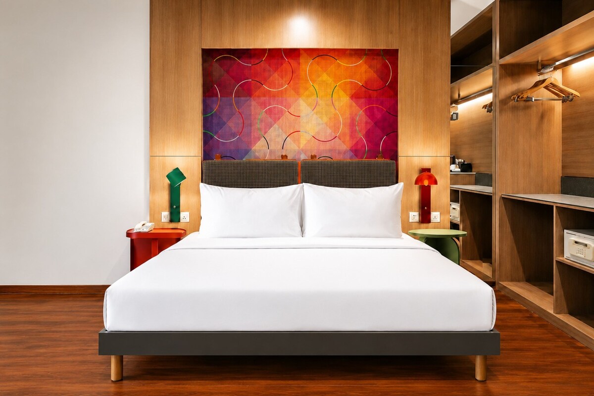 Ein Hotelzimmer mit Bett, Nachttisch, Wandlampe und Kleiderschrank.