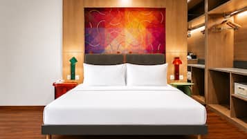 A hotel room with a bed, a nightstand, a bedside table, a wall-mounted lamp, and a wardrobe.