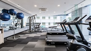 Ein modernes Fitnessstudio mit Trainingsgeräten, darunter Laufbänder und ein Kraftgerät, und ein großes Fenster mit Blick auf die Stadt.