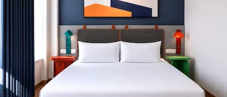 Una habitación de hotel moderna con una cama grande, un cabecero con diseño geométrico, una mesita de noche con lámpara y una obra de arte colgada en la pared.