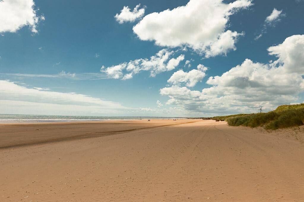 A wide sandy beach with a clear sky and scattered clouds.