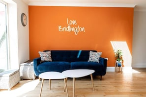 A living room with a dark blue sofa, two white round tables, and an orange wall with "Love Bridlington" written on it.