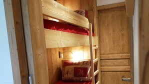 A wooden bunk bed room with a red blanket, a small table with a decorative pillow, and a wooden wardrobe. - Newly renovated apartment. It is located 150 metres from the slopes, opposite the comm (Montvalezan)