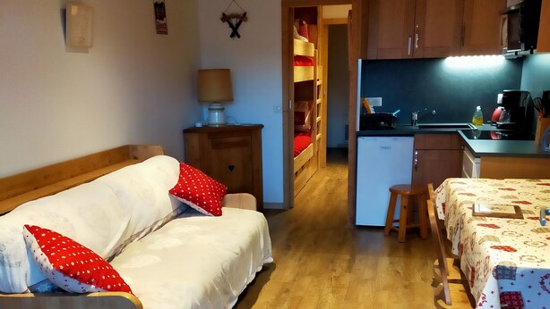 A cozy room with a wooden sofa, a small table, and a kitchen area with a fridge and sink. - Newly renovated apartment. It is located 150 metres from the slopes, opposite the comm (Montvalezan)
