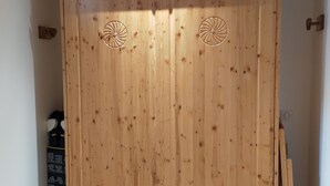 A wooden wardrobe with two circular designs on the doors, a small shelf, and a box of items on the floor. - Newly renovated apartment. It is located 150 metres from the slopes, opposite the comm (Montvalezan)
