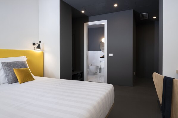 A modern hotel room with a bed, a bedside lamp, and a view into the bathroom. - Camplus Hotel Roma Centro (Rome)