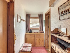 Ein gemütliches Zimmer mit einer hölzernen Sitzbank, einem kleinen Tisch mit einem Korb, einem Holzschrank und einem Regal mit diversen Gegenständen.